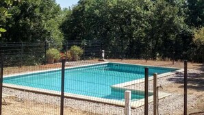 Ein rechteckiger Pool, umgeben von einem Drahtzaun, mit einem Holzdeck im Vordergrund und Bäumen im Hintergrund.