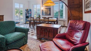 Una sala de estar acogedora con un sofá verde, un sillón de cuero rojo, un aparador de madera y una mesa de comedor con sillas.