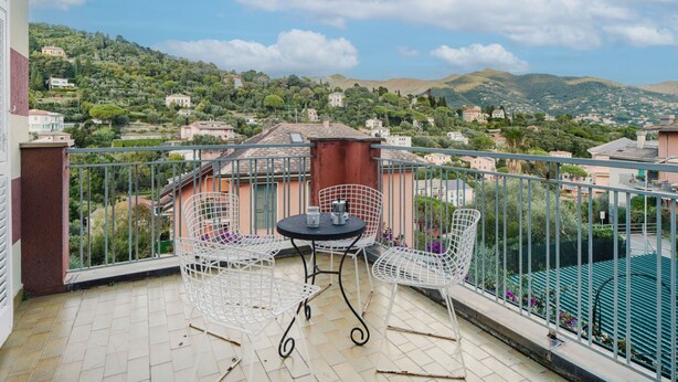 Un balcón con una mesa y dos sillas, con vistas a una colina con casas y vegetación.