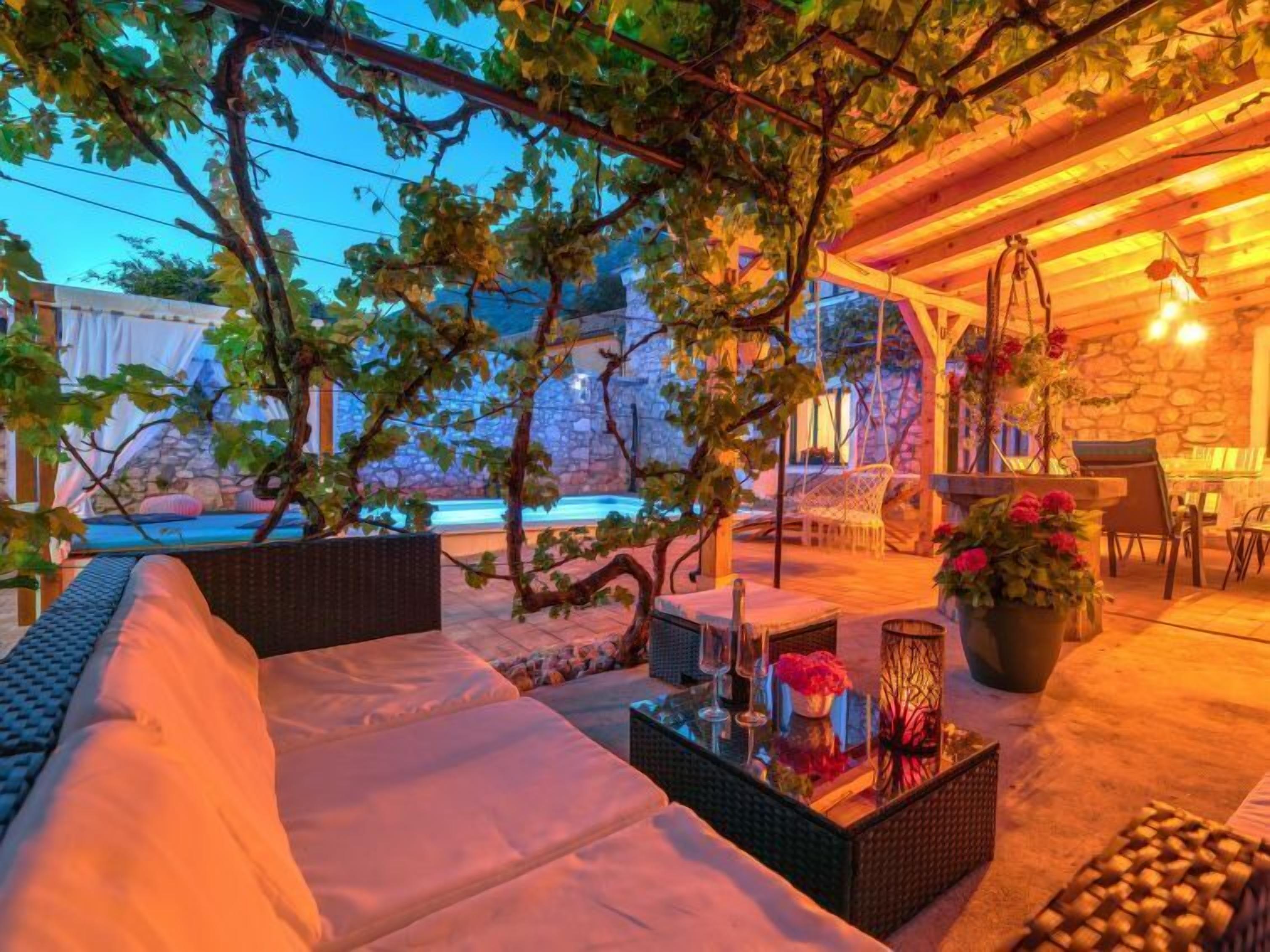 A cozy outdoor seating area with a pool, stone walls, and hanging plants.