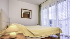 A bedroom with a bed, a nightstand, a lamp, a mirror, and a window with curtains. - Apartment File by Interhome (Umag/Zambratija)