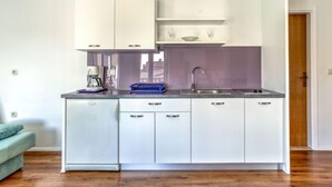 A compact kitchen with white cabinets, a built-in dishwasher, and a purple backsplash. - Apartment File by Interhome (Umag/Zambratija)