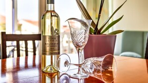 A bottle of Vina Istria Malvasija Istarska wine, a wine glass, and a broken wine glass on a table with a wooden chair and a potted plant in the background. - Apartment File by Interhome (Umag/Zambratija)