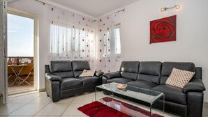 Una sala de estar moderna con un sofá de cuero negro, una mesa de centro de vidrio y un tapete rojo. Se ve un balcón con una mesa y sillas a través de la ventana.