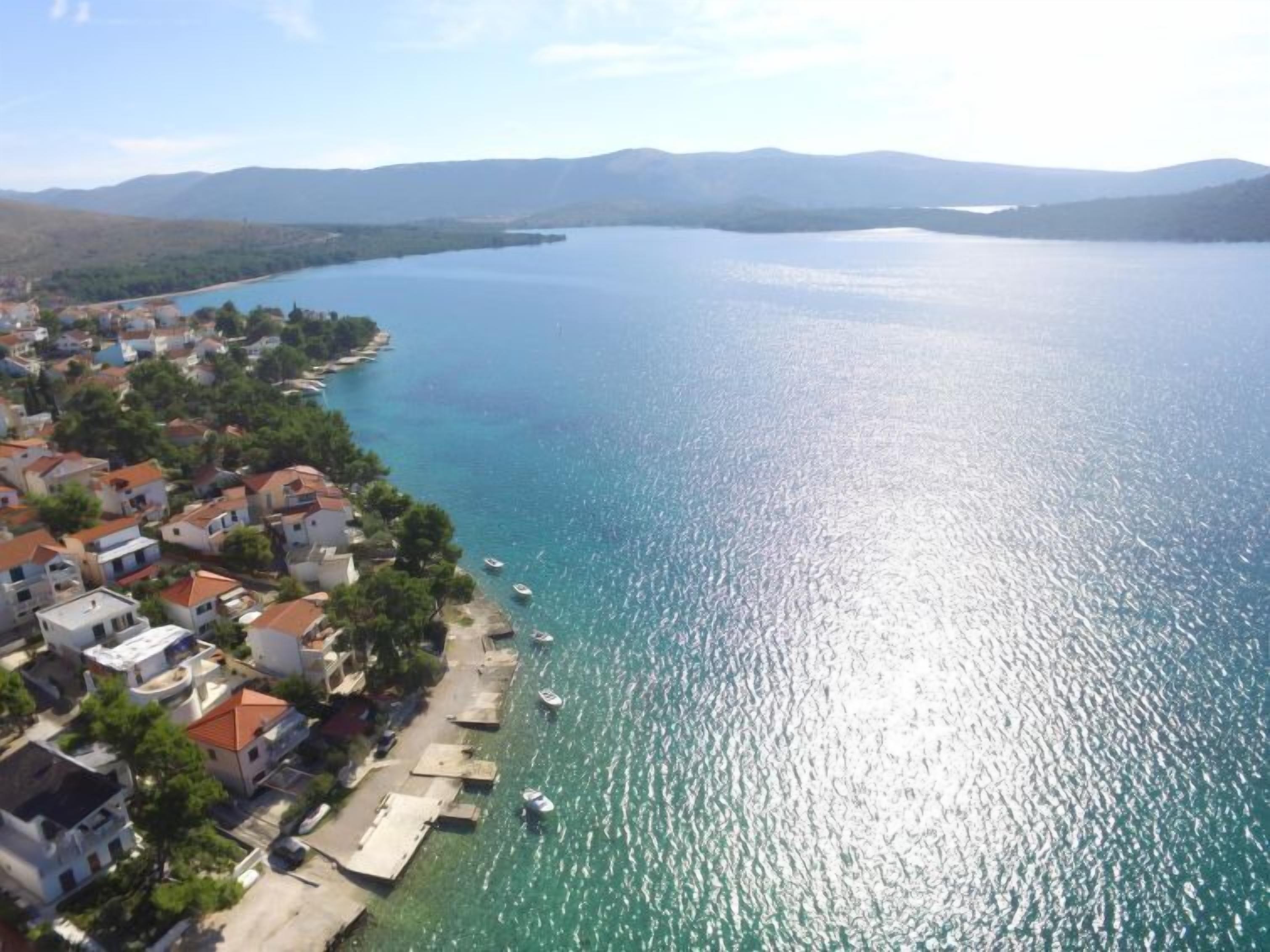 An aerial view of a coastal town with houses along the shoreline, boats in the water, and mountains in the background.