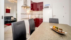 Una cocina moderna con armarios rojos, un refrigerador blanco y una zona de comedor con mesa de madera y sillas negras.