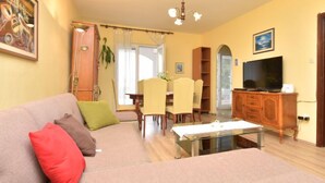 Una sala de estar con un sofá, una mesa de centro de vidrio, un televisor y un comedor con sillas y una mesa.
