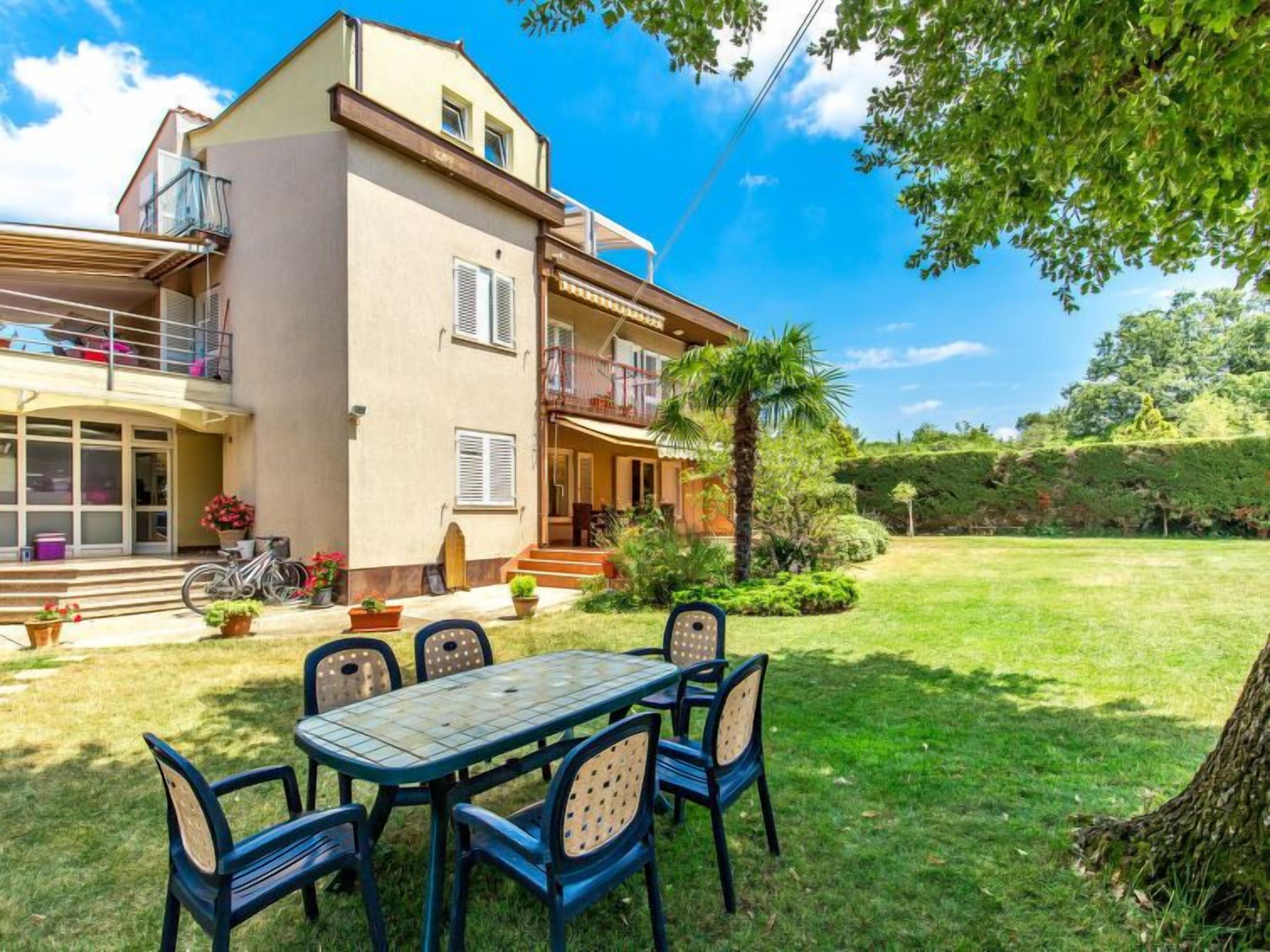 Una casa de dos pisos con un balcón, un patio con mesa y sillas, y un césped bien cuidado.
