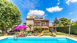 A swimming pool with lounge chairs and umbrellas, surrounded by a two-story building with balconies. - Apartment Silva by Interhome (Fažana/Peroj)