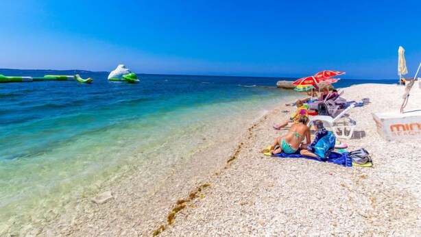 A beach with clear water, a few people relaxing, and a lifeguard tower in the background. - Apartment Silva by Interhome (Fažana/Peroj)
