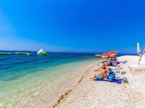 Una playa con agua cristalina, algunas personas relajándose y una torre de salvavidas al fondo.