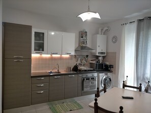 Cucina compatta con forno a microonde, forno e lavello. Presente un tavolo da pranzo con sedie e un lampadario.