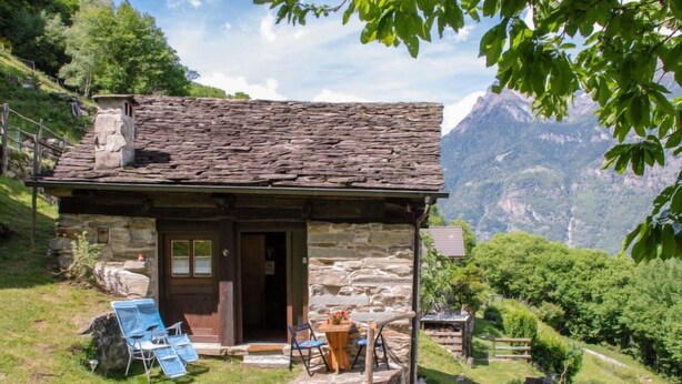 Un rustico in pietra con una porta in legno e un piccolo portico.