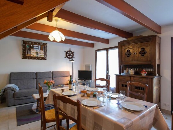 A dining area with a table set for four, a sofa, a television, and a wooden cabinet with kitchenware.