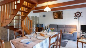 A dining area with a table set for four, a wooden staircase, a grey sofa, and a television in the living area. - Ty Pendruc by Interhome (Tregunc)
