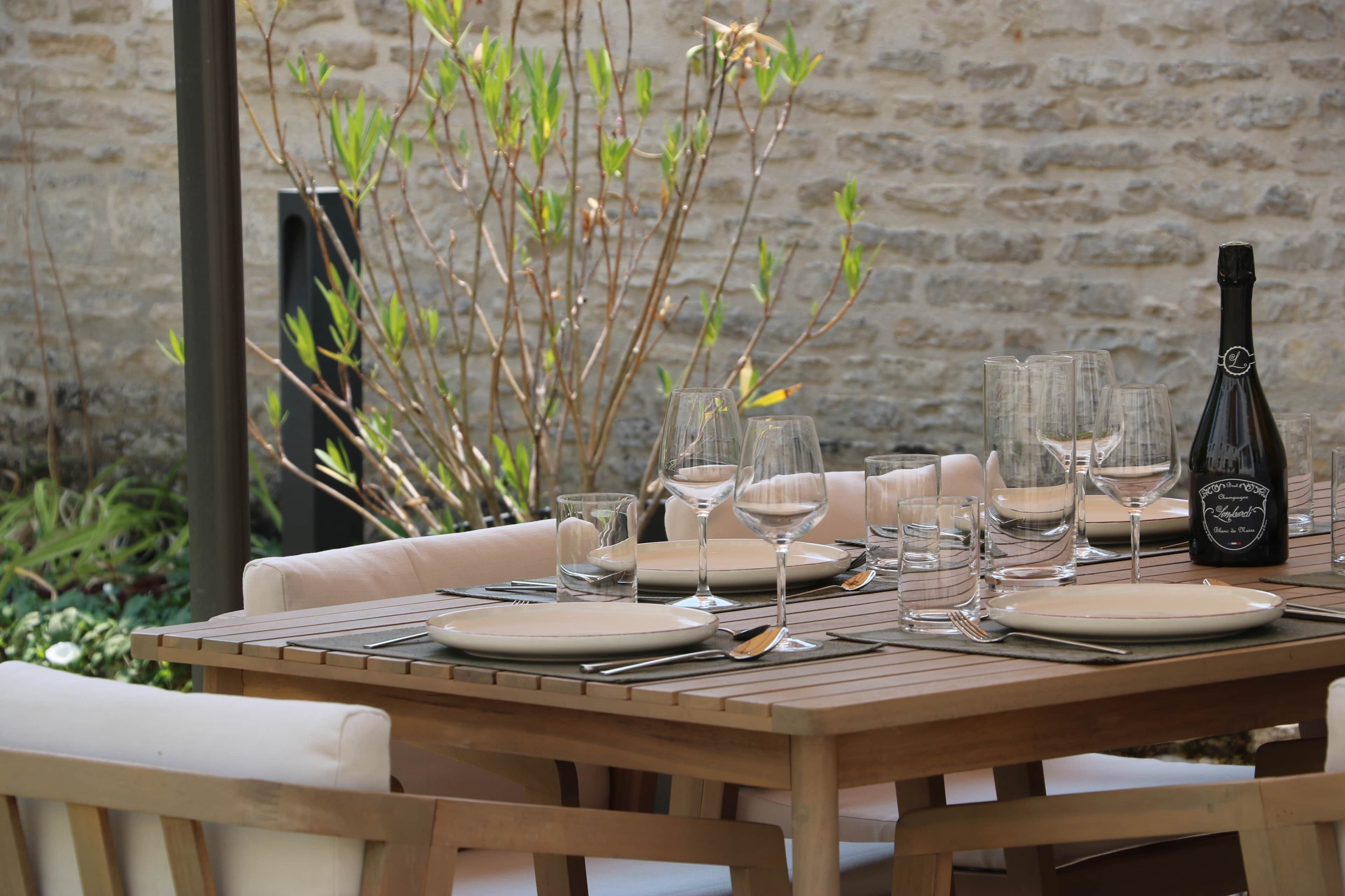 Une table de salle à manger en bois, mise avec des assiettes, des verres et des couverts, accompagnée d’une bouteille de champagne.