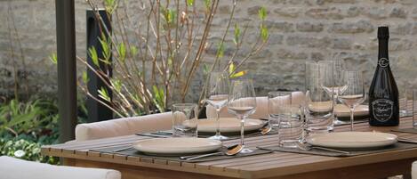 A wooden dining table set with plates, glasses, and cutlery, accompanied by a bottle of champagne.