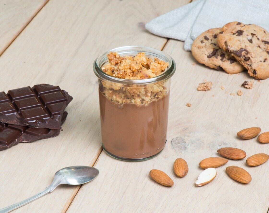 A glass jar with a chocolate dessert, a chocolate bar, and cookies on a wooden surface.