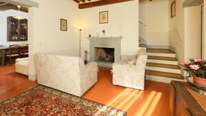 Una sala de estar con chimenea, dos sofás, un tapete estampado y una escalera.