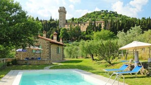 Una piscina con sillones de descanso, un edificio de piedra y un castillo al fondo.