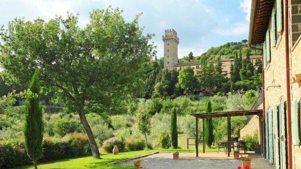 Un patio con un sendero de grava, plantas en macetas y un edificio con una torre de piedra al fondo.