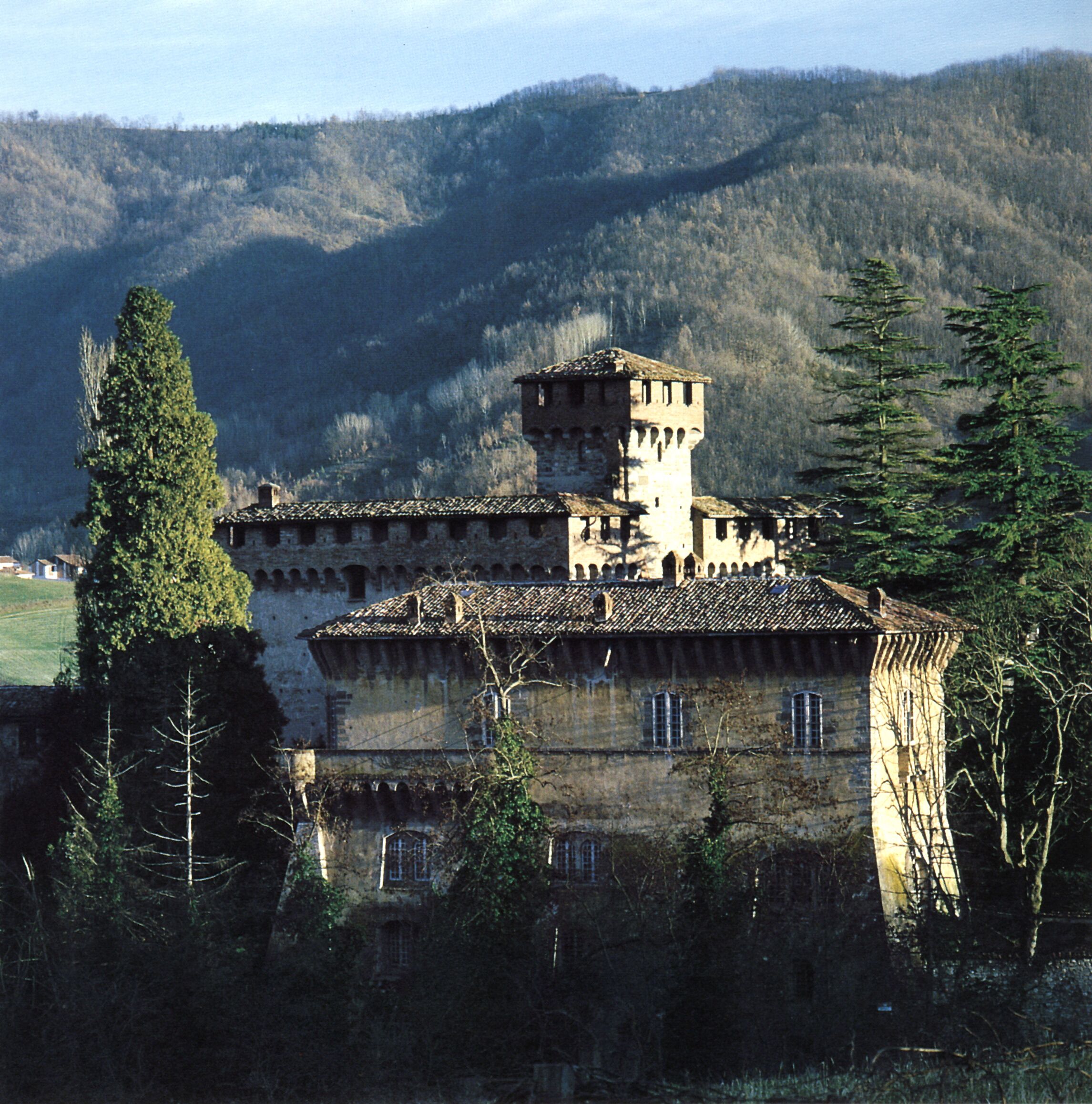 A historic building with a tower, surrounded by trees and hills.