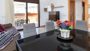 Een moderne woonkamer met een glazen eettafel, grijze stoelen, een bank en een televisie.