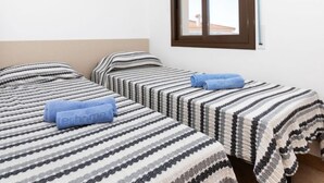 Een kamer met twee bedden, elk met gestreept beddengoed en een blauwe handdoek. Er is een raam met uitzicht op gebouwen.