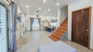 A spacious living area with a staircase, a dining table, and a TV mounted on the wall. - Sanssouci Kep (Kep)