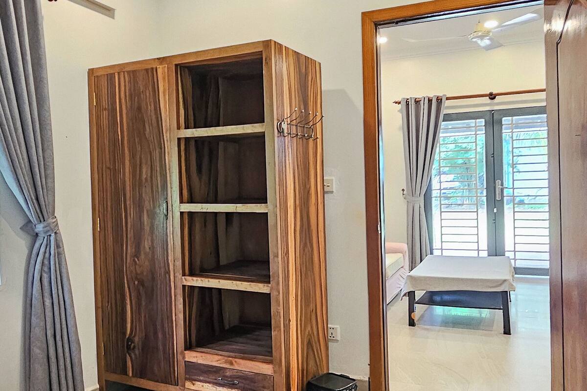 A bedroom with a wooden wardrobe, a bed with a white duvet, and a view through an open door to a balcony.
