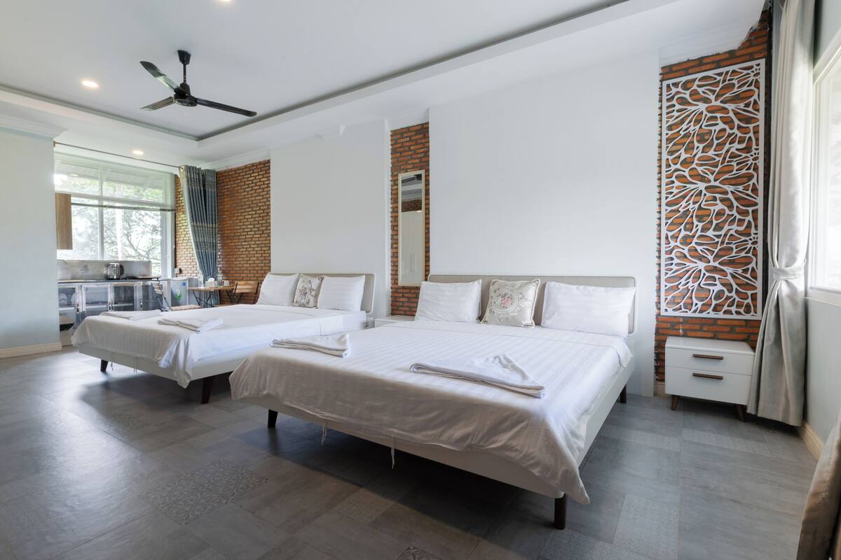 A modern hotel room with two beds, a ceiling fan, a brick accent wall, and a decorative panel.