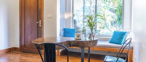 Comedor con una mesa redonda de madera, dos sillas negras, una planta en maceta y una ventana con vistas al verdor.