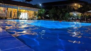 A swimming pool with a tiled deck, surrounded by outdoor seating and a building with a tiled roof. - Sanssouci Kep (Kep)