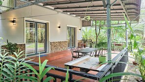 A covered patio area with a table and chairs, a stone wall, and potted plants. - Sanssouci Kep (Kep)