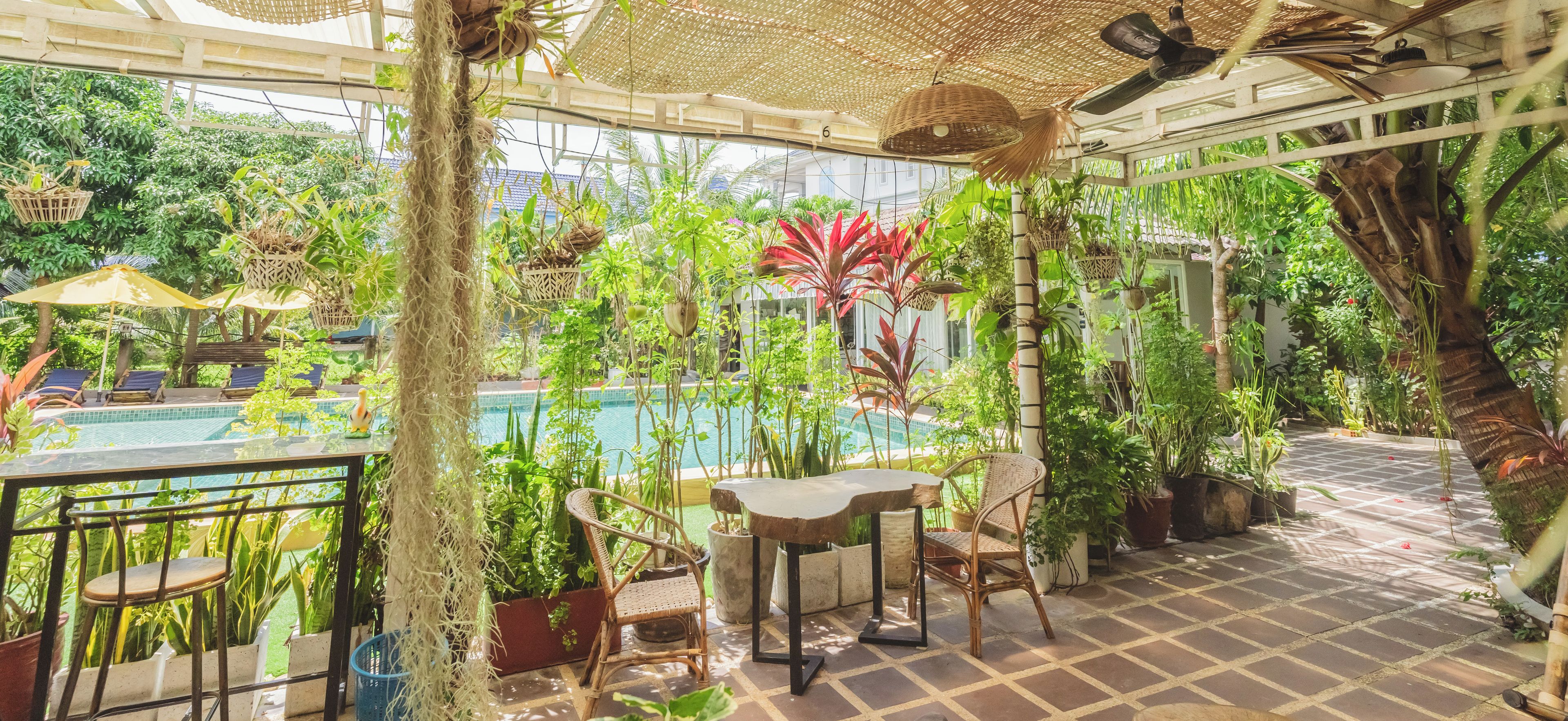 A poolside area with a table and chairs, surrounded by lush greenery and potted plants.