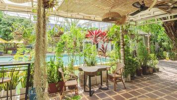 A poolside area with a table and chairs, surrounded by lush greenery and potted plants.