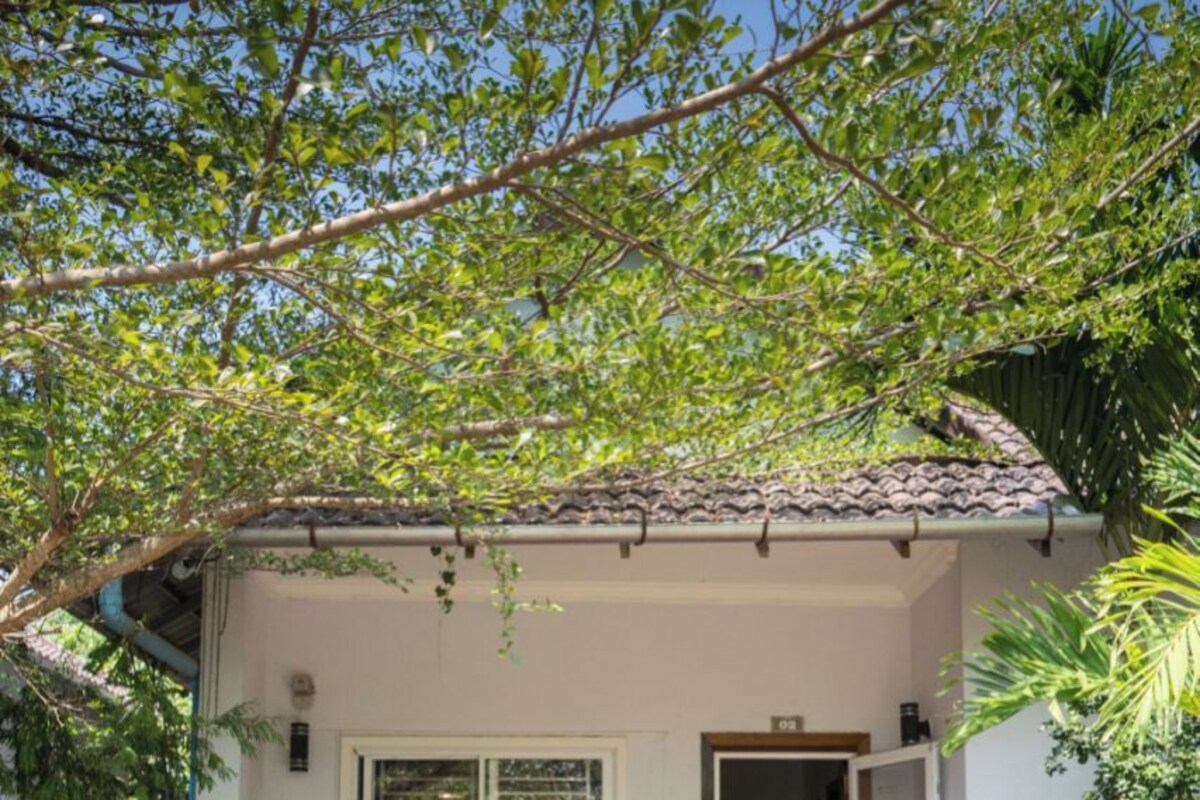 A small, single-story house with a tiled porch, two wicker chairs, and a door leading to an interior room.