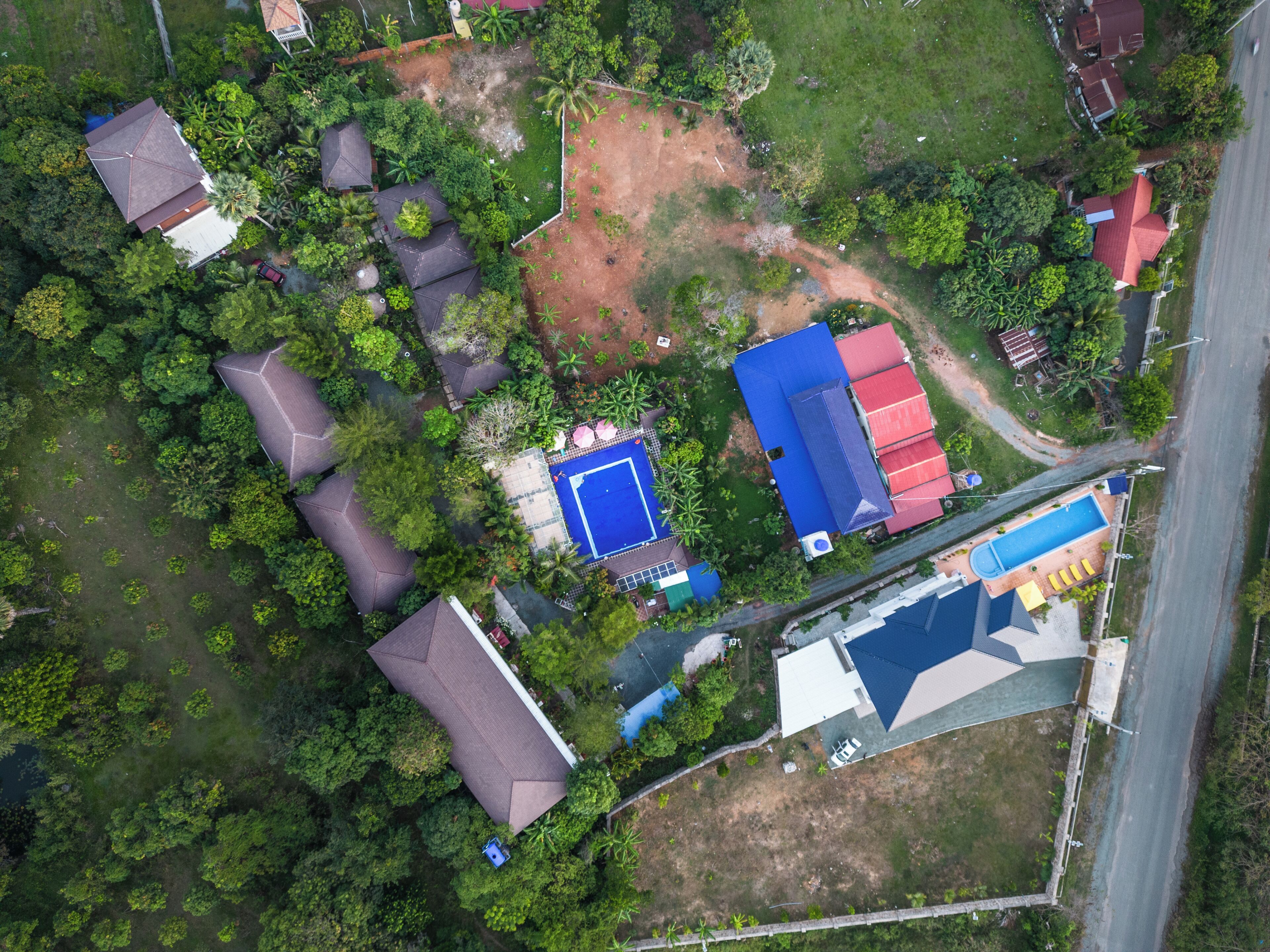 An aerial view of a residential area with multiple houses, a swimming pool, and surrounding greenery.