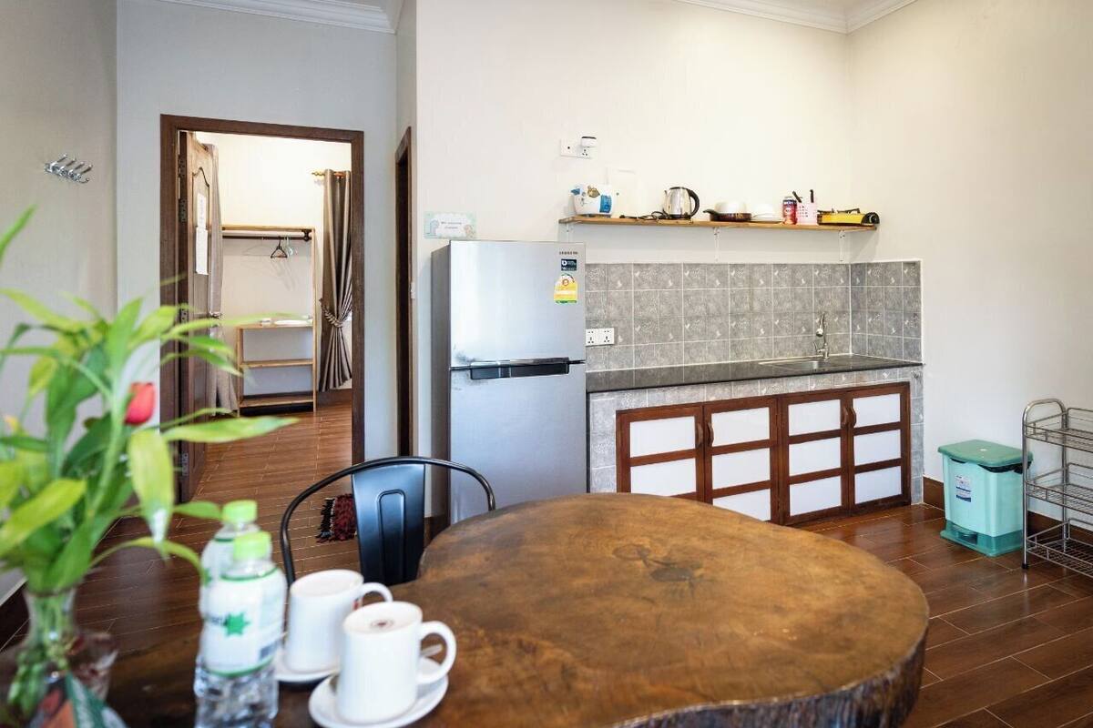 A compact kitchen with a refrigerator, a sink, and a wooden cabinet. There is a dining table with chairs and a vase with flowers.