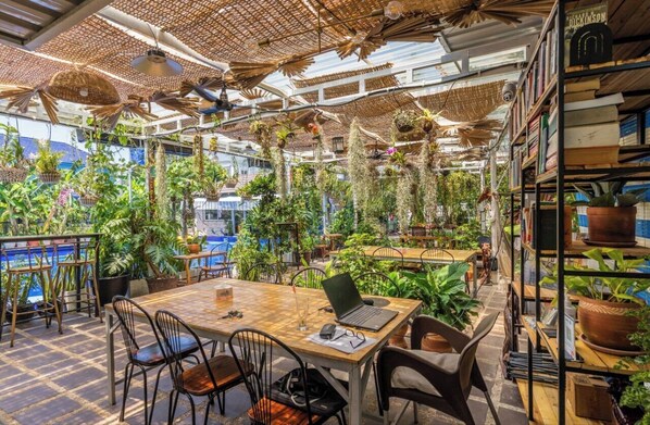 An indoor space with tables and chairs, surrounded by shelves with books and potted plants. - Sanssouci Kep (Kep)