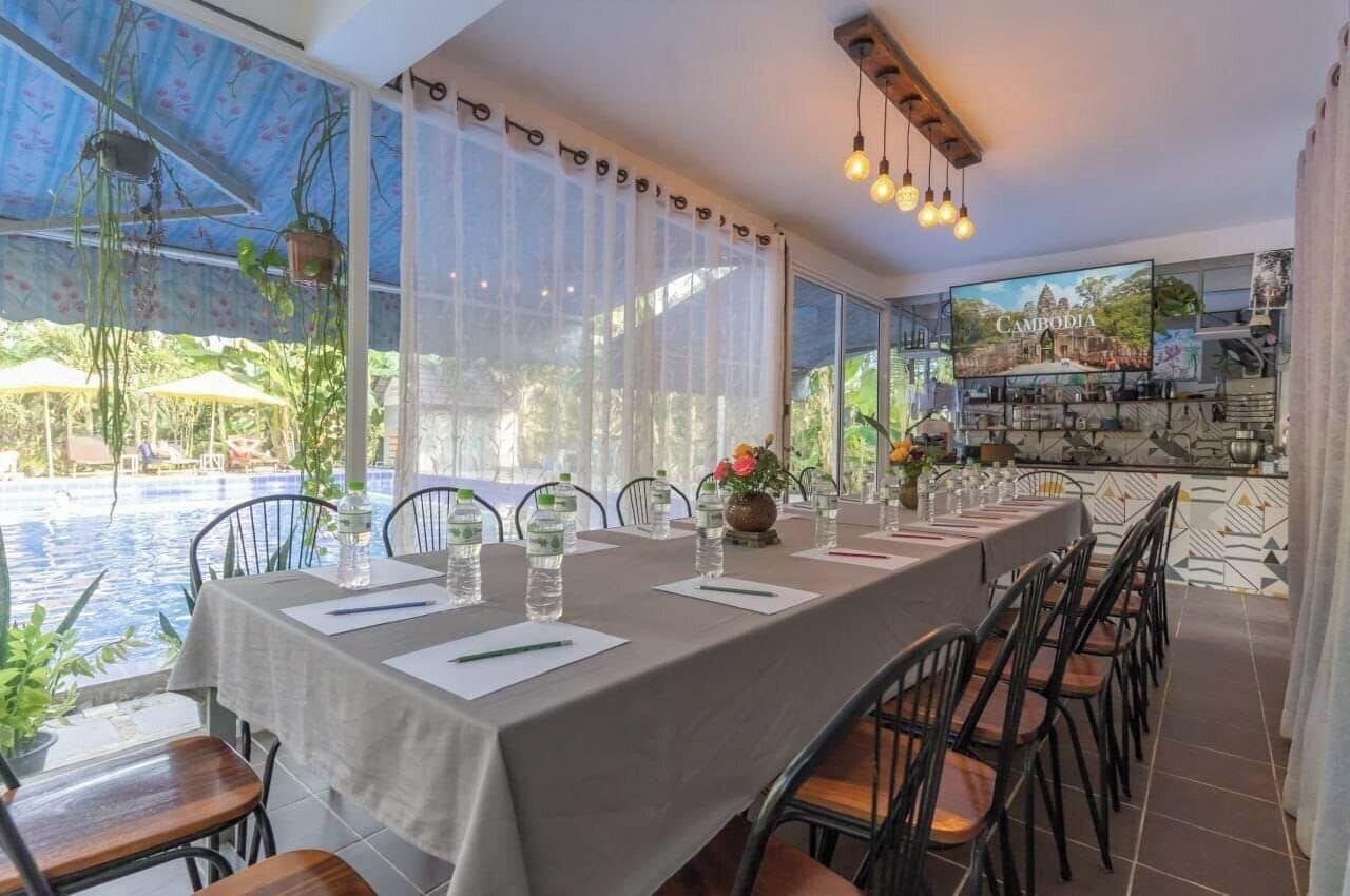 A dining area with a long table set for a meal, large windows with curtains, and a pool visible outside.