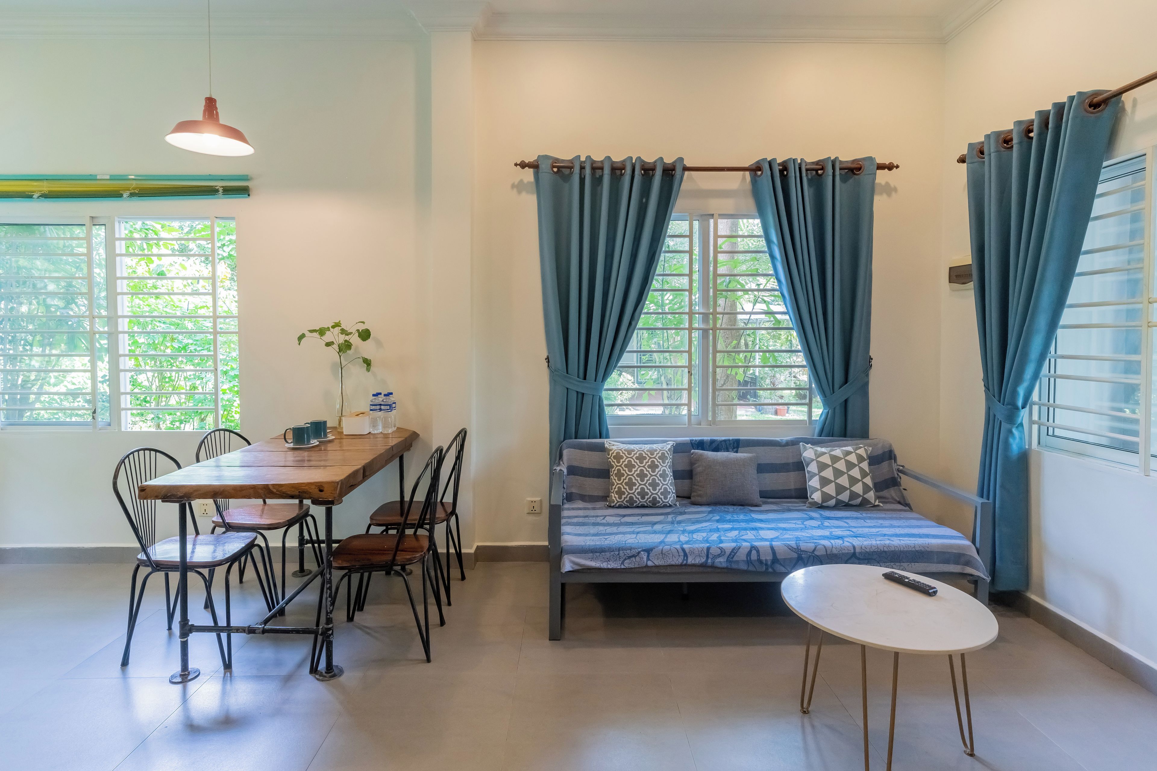 A room with a dining table, chairs, a sofa, a small round table, and a hanging light fixture.