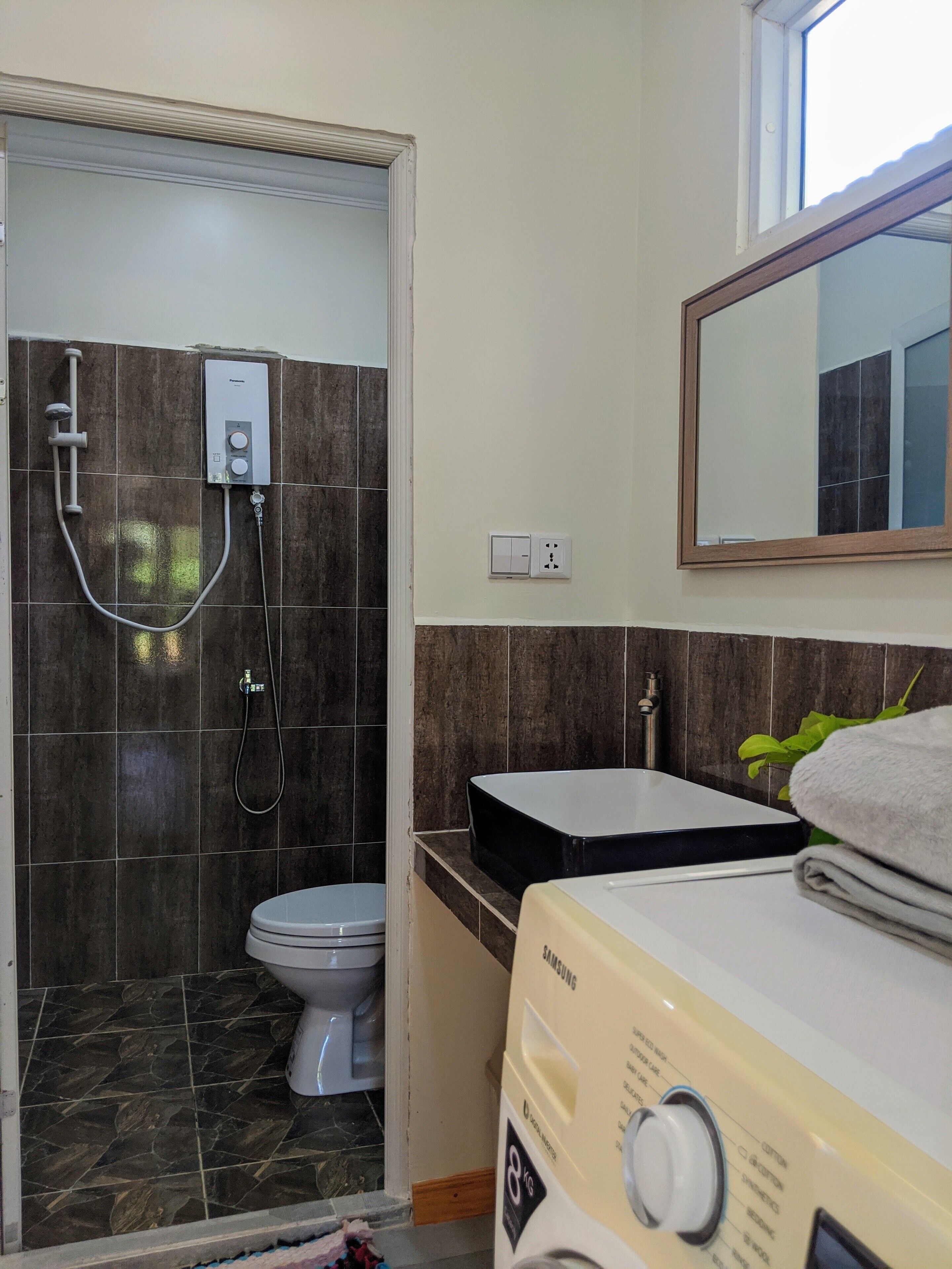 A bathroom with a shower, toilet, and a Samsung washing machine.
