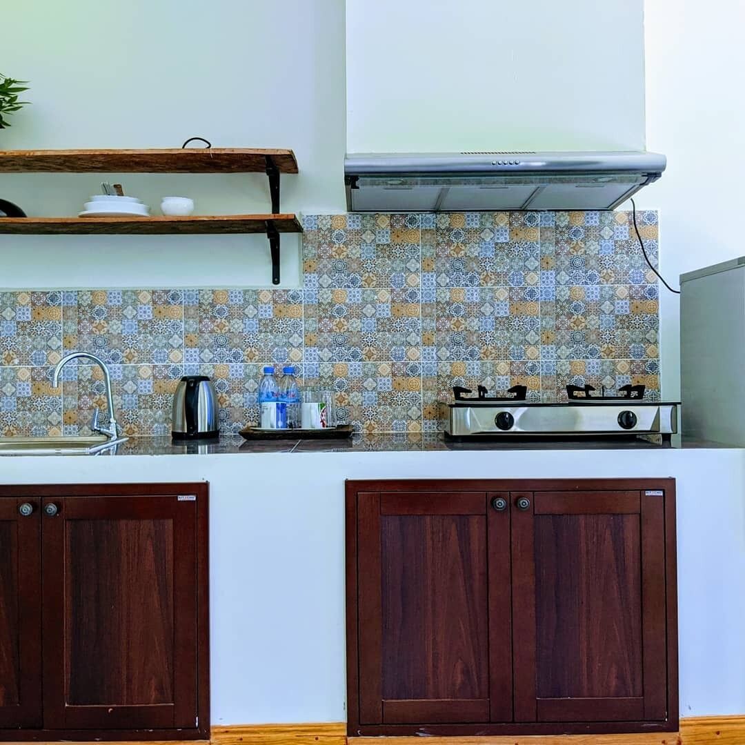 A kitchen with a gas stove, wooden cabinets, a tiled backsplash, and a shelf above the sink.