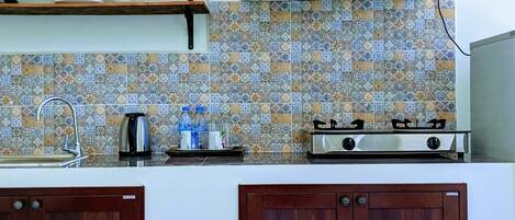 A kitchen with a gas stove, wooden cabinets, a tiled backsplash, and a shelf above the sink.