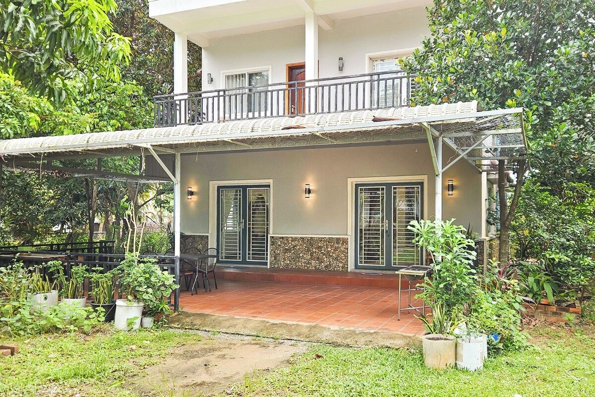 A two-story house with a balcony, a covered porch, and a garden area with potted plants.