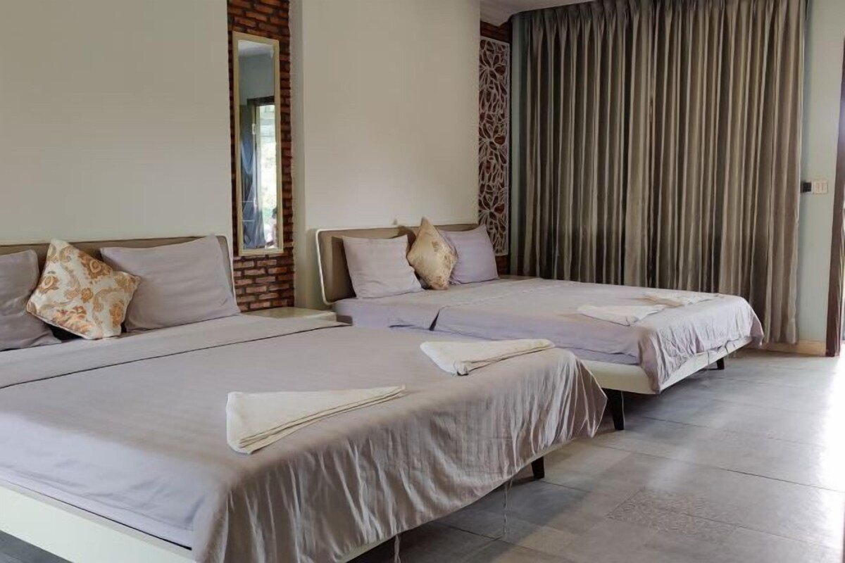 A hotel room with two beds, each with a white bedspread and pillows, a brick accent wall, a mirror, and a curtain.