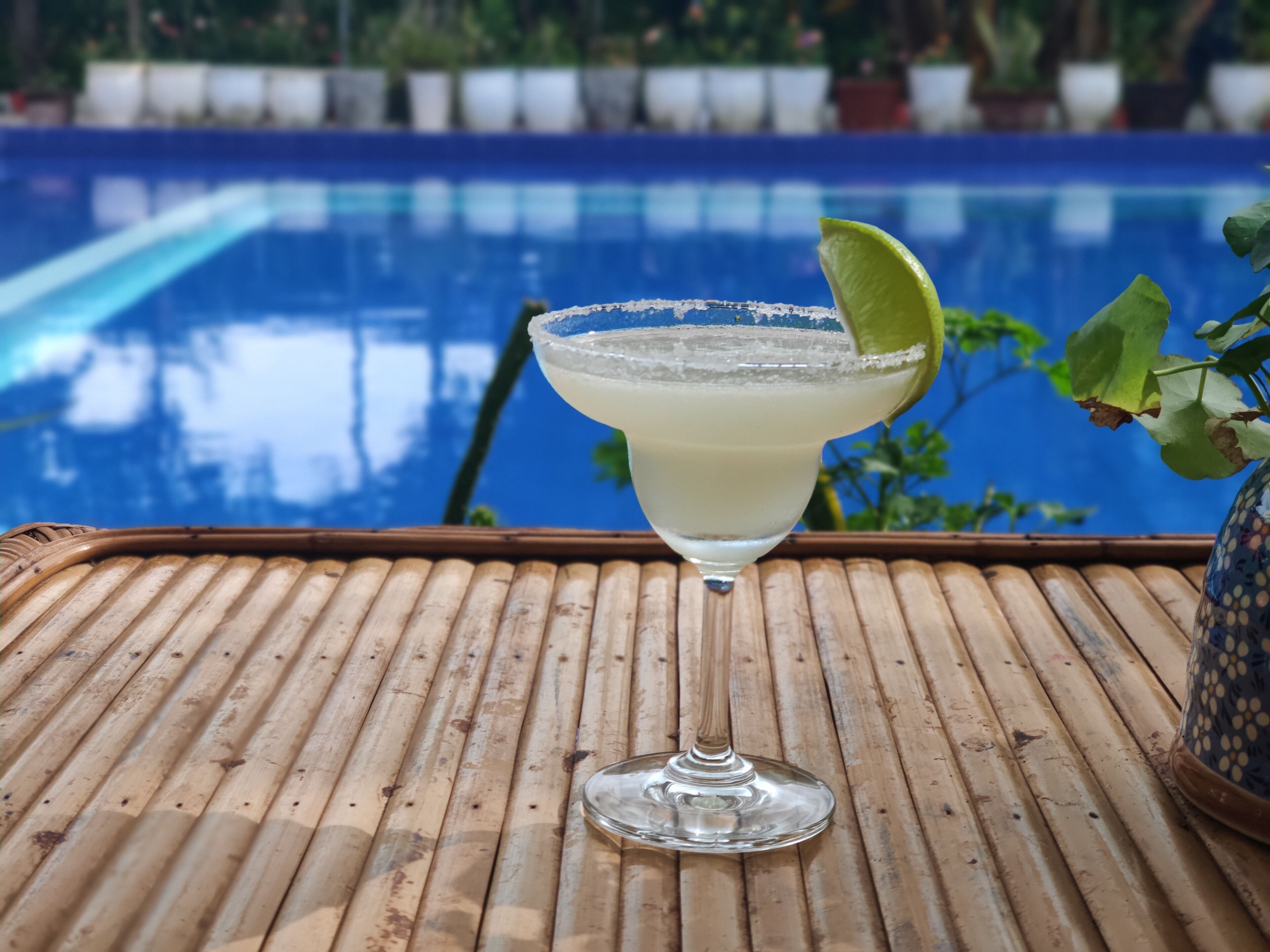 A cocktail glass with a lime garnish on a bamboo mat by a pool.