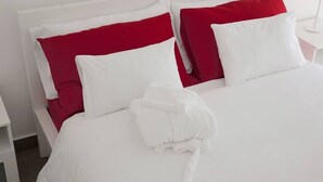 A neatly made bed with white and red bedding, a white robe on the bed, and a white nightstand with a lamp. - Domus Claudiae's studio C-1 (Catania)
