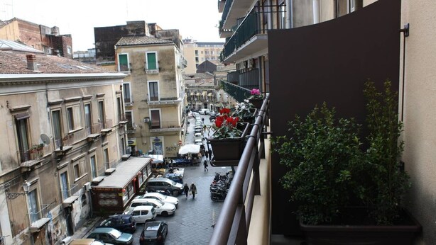 A narrow street with parked cars and buildings on either side. - Domus Claudiae's studio C-1 (Catania)